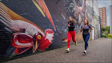 Twee vrouwen rennen langs één van de Mauritshuis Murals in Den Haag.